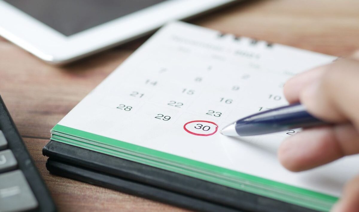 Hand, die mit einem Stift einen Termin im Kalender ankreuzt