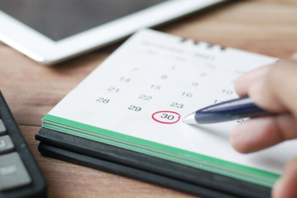 Hand, die mit einem Stift einen Termin im Kalender ankreuzt